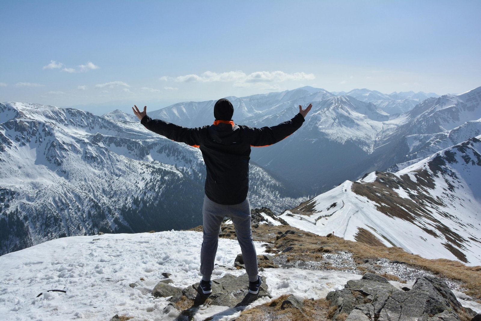 A man stands on a snowy mountain peak with arms raised, embracing the breathtaking view.
